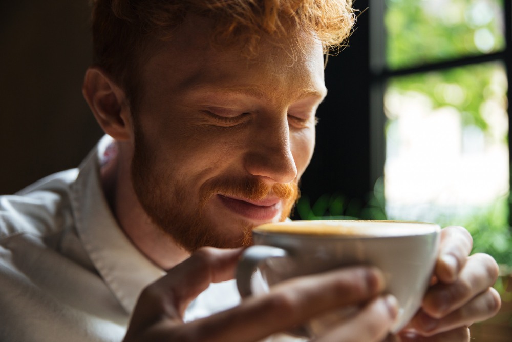 Un homme barbu renifle du café en fermant les yeux.